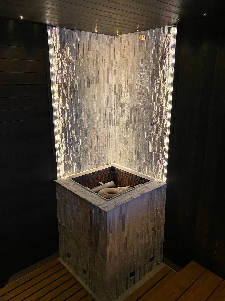 Чёрная «Богатырь-баня» в Боровске: четыре уровня полков, белый кварцит в противопожарном углу и кастомная газовая печь в центре внимания. SaunaTopMasters