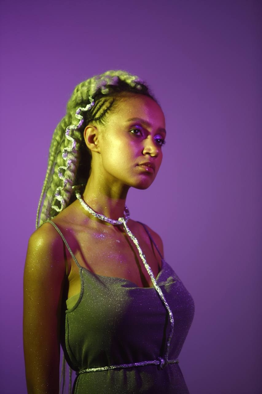 Космическая фотосъёмка девушки в фиолетовом свете с яркими косичками.