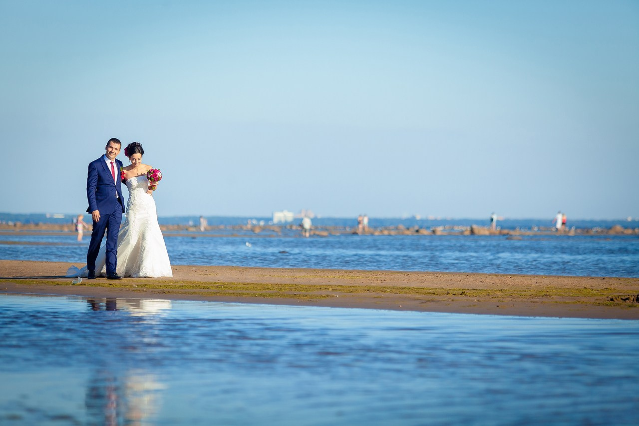 жених и невеста с красным букетом гуляют вдоль берега Финского залива