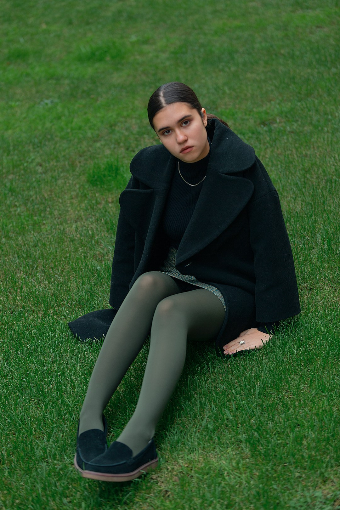Девушка сидит на траве в чёрной одежде — минимализм и чистый фон