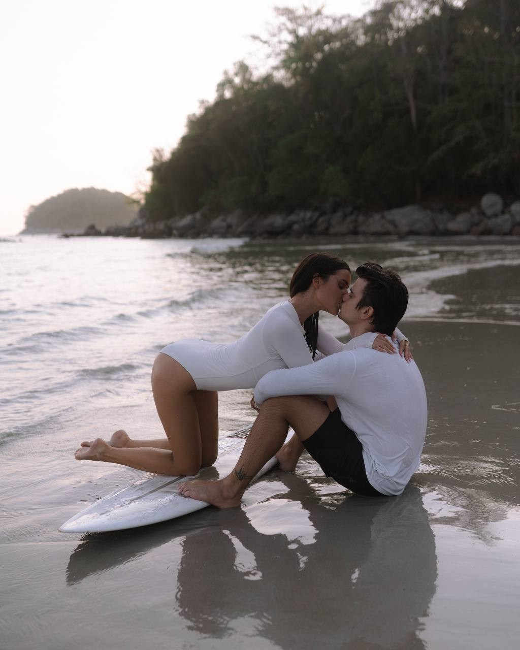 Пара сидит на песке рядом с доской — семейная фотосессия на пляже