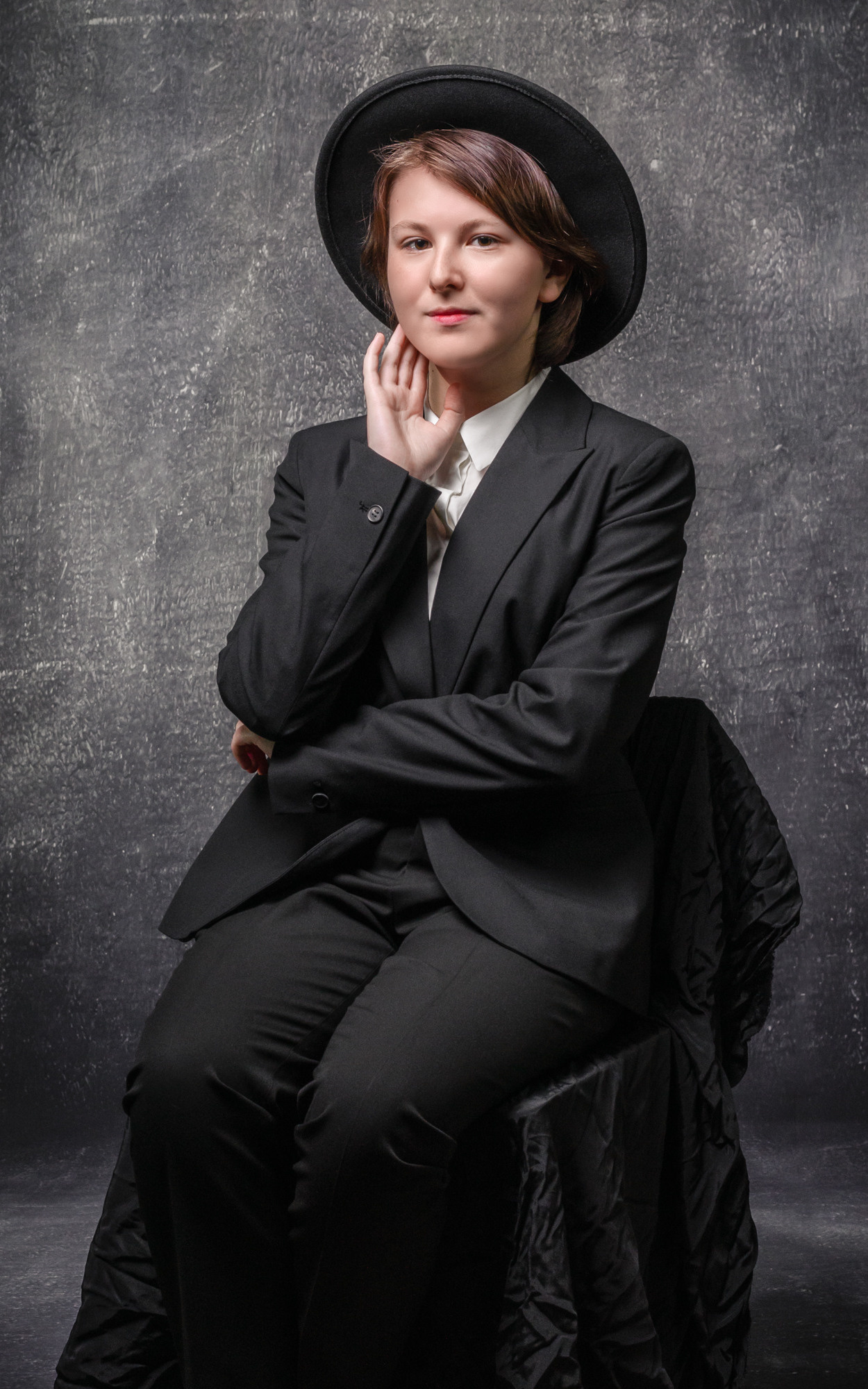 Художественный портрет школьницы в шляпе и черном костюме на фотофоне в классе.