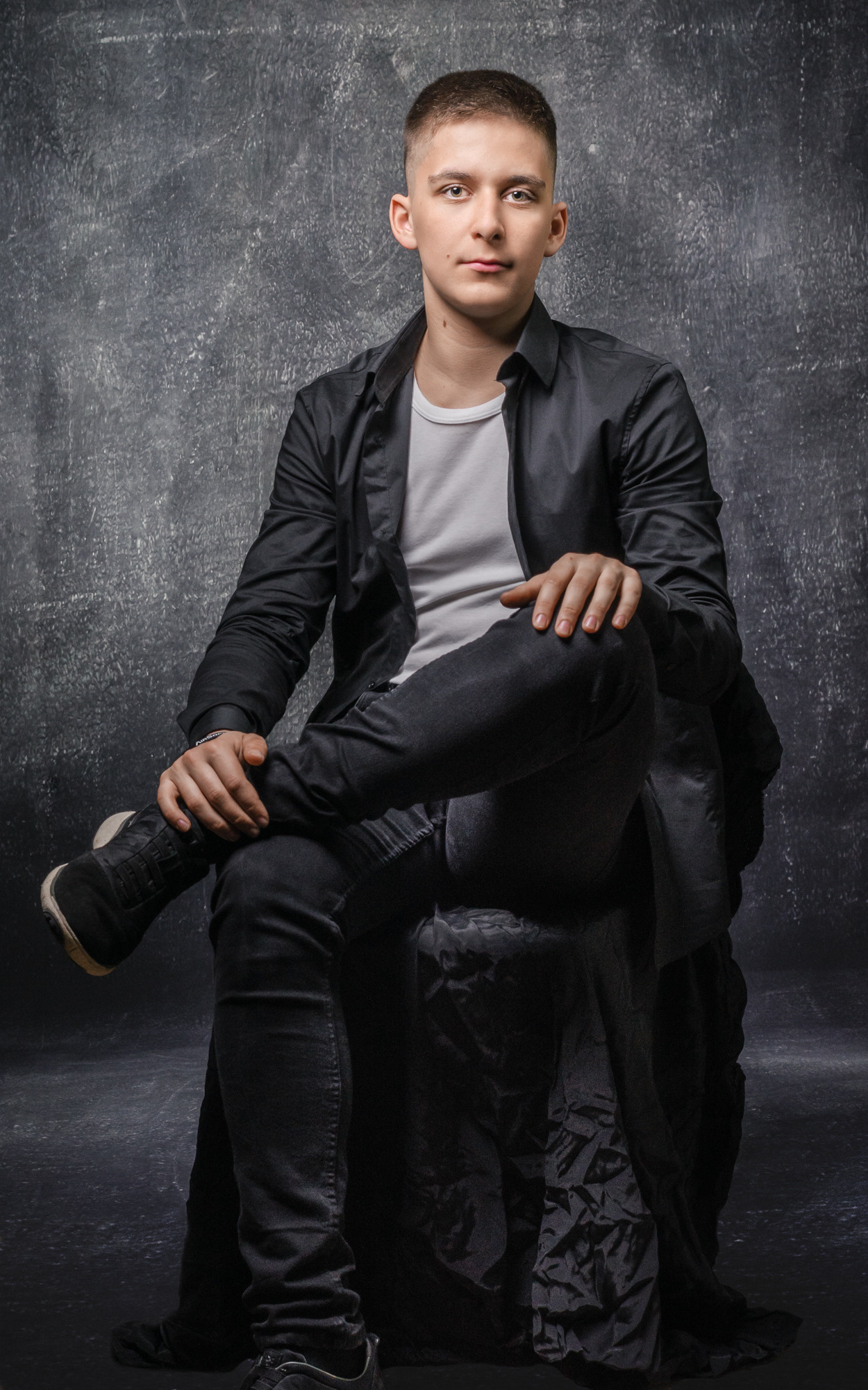 Ученик на фотосессии в черном костюме на черном фоне.