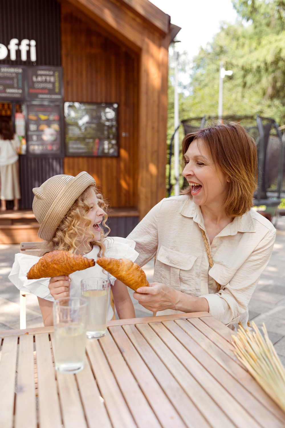 Мама с дочкой  за столом  возле кафе кушают пирожки.