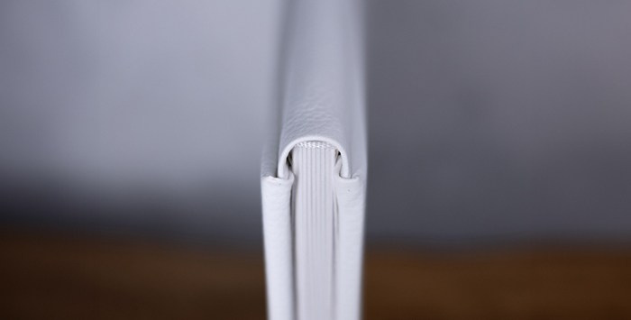 Крупный план переплета фотокниги из белой кожи. Идеально ровный корешок и плотное прилегание страниц — залог долговечности семейного архива.