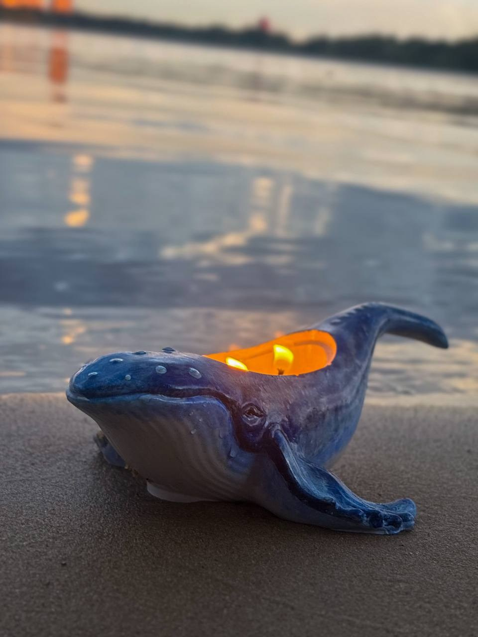 Фото синей свечи в форме дельфина, горящей на фоне закатного неба.