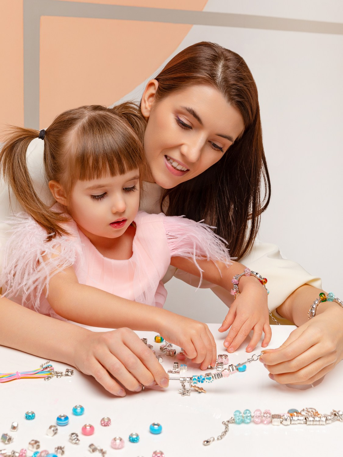 Мама с дочкой сидят за столом и собирают бусы.