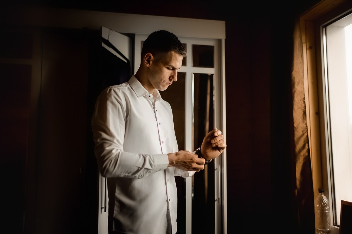 Жених застёгивает пуговицы рубашки  в комнате в Санкт-Петербурге. Горизонтальный кадр
