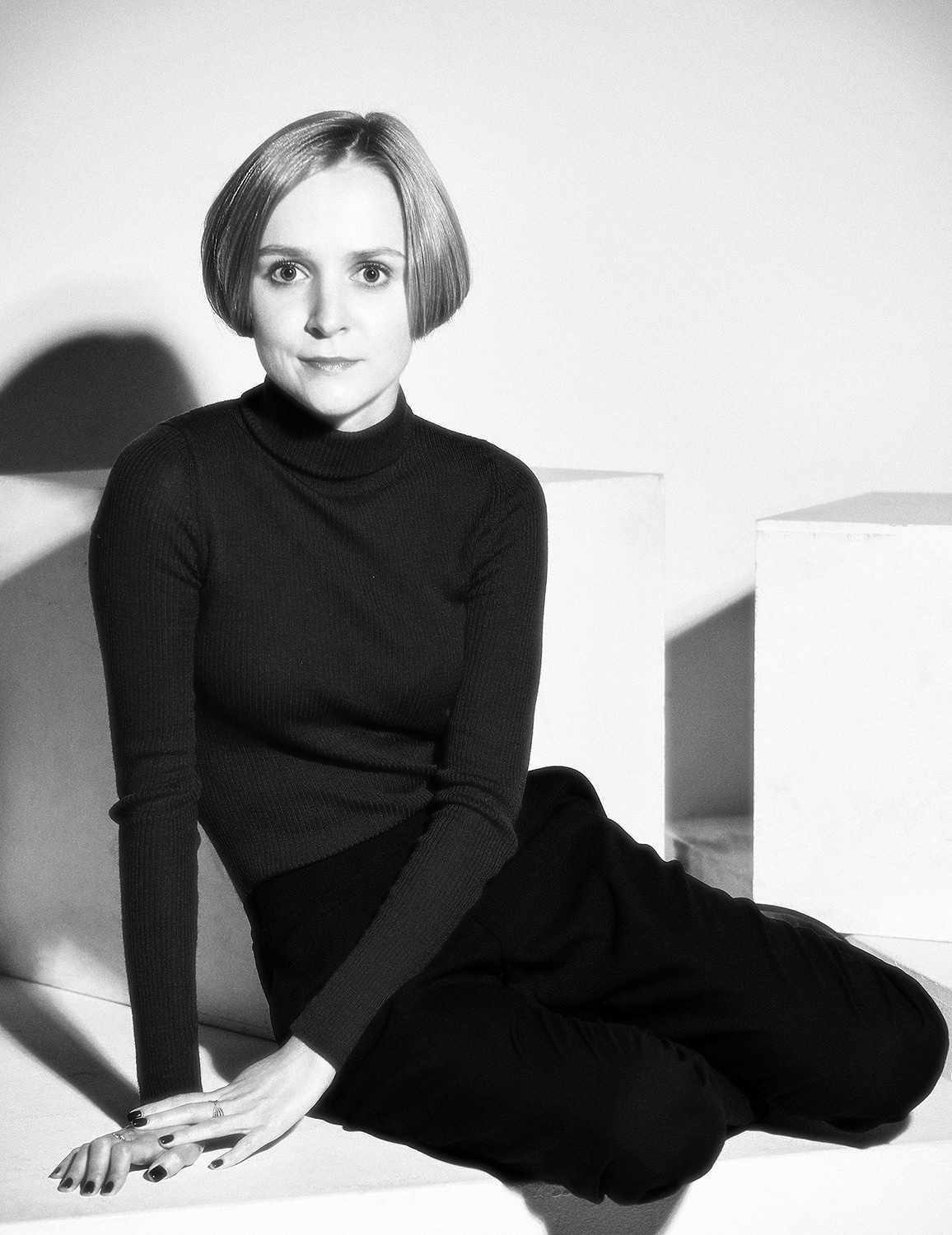 чёрно-белый портрет молодой женщины со светлыми волосами, в чёрном свитере, сидящей на полу