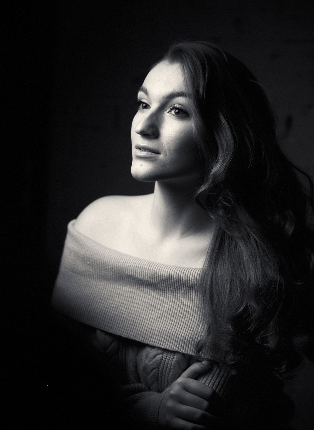 чёрно-белый портрет молодой женщины в свитере с чёрными распущенными волосами на тёмном фоне