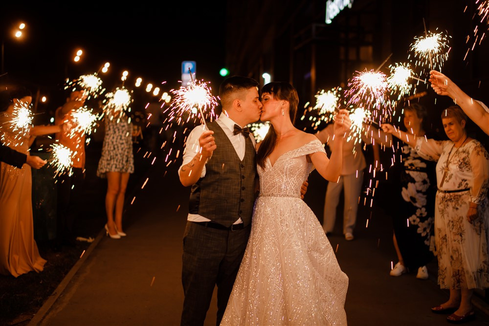 Свадебное фото с бенгальскими огнями. Гости держат бенгальские огни, жених с невестой целуются.