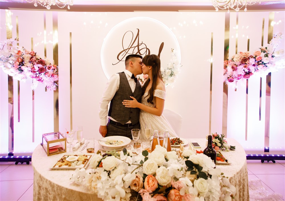 Жених и невеста целуются за свадебным столом.