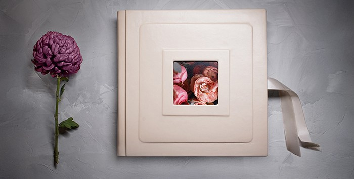 Эстетичная композиция: фотокнига в светлой кожаной обложке расположена рядом с крупным фиолетовым цветком на сером фактурном фоне.