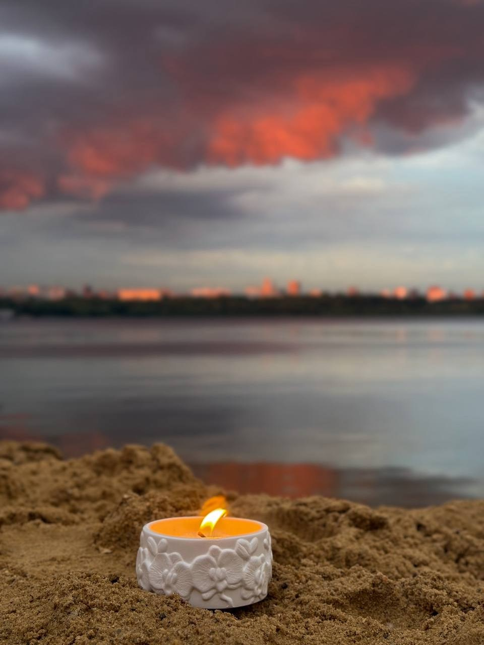 Свеча в керамической банке на песке у воды — закатная фотосессия.