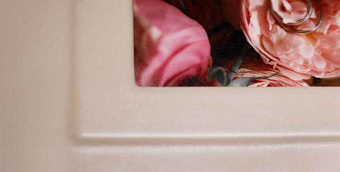 Деталь обложки фотокниги: вставка фотографии с обручальными кольцами и розами под защитным покрытием, обрамленная аккуратным паспарту.