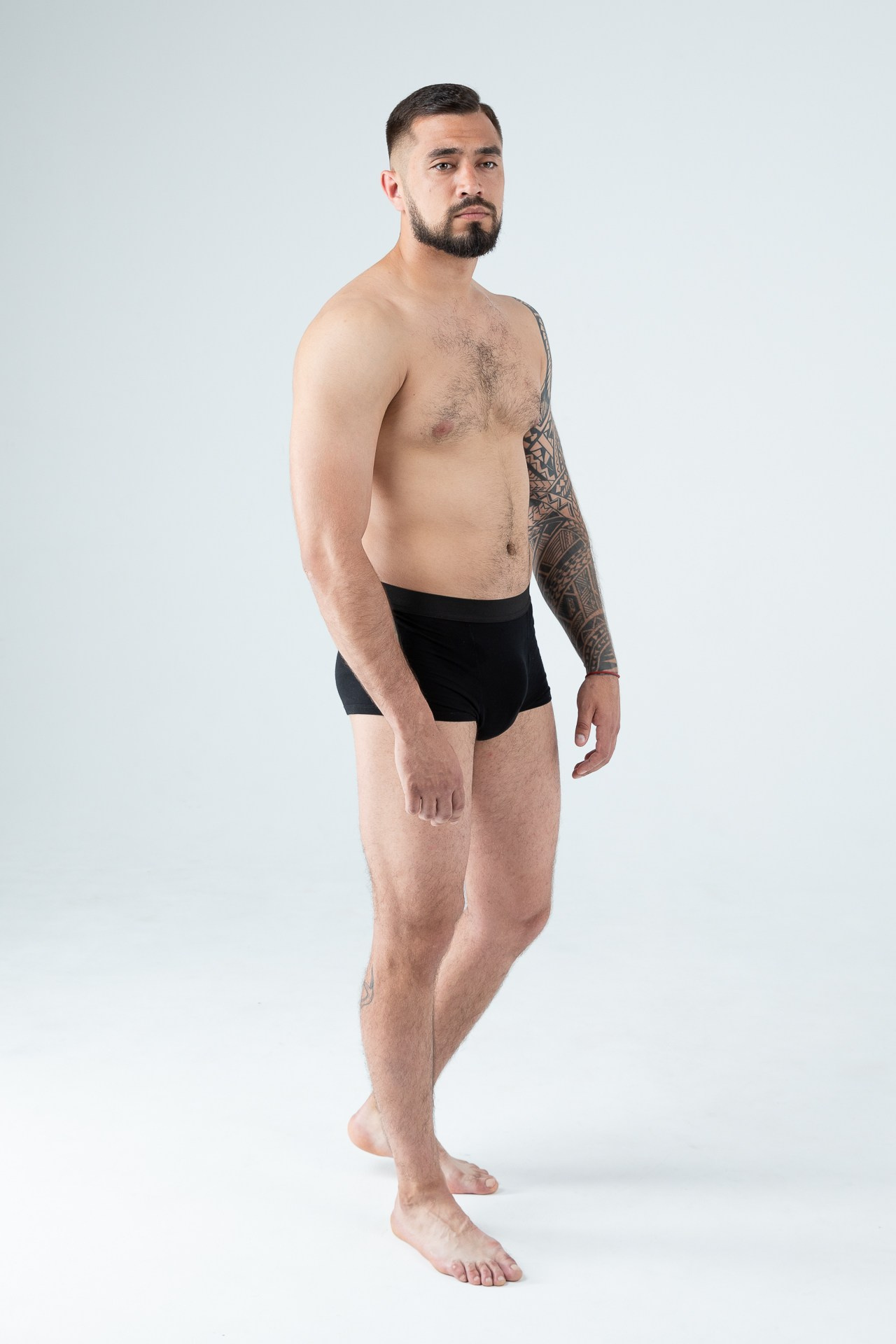 Мужчина модель с бородой с татуировками в черных трусах
