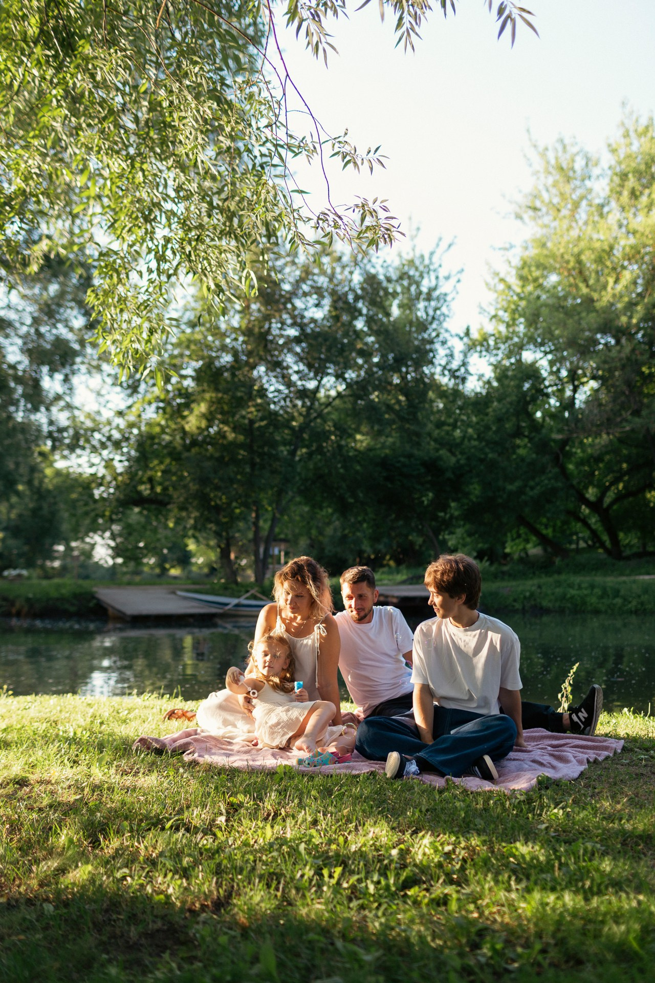 Семья из четырех человек сидит на берегу озера. Семейный летний пикник у воды.