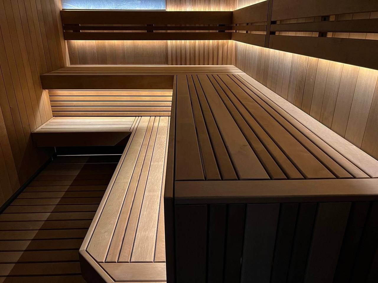 Сауна в Керро из разноширокой термоольхи. Ламповый свет термостойких лент и закарнизная подсветка плитки из талькохлорита 300×300мм. SaunaTopMasters