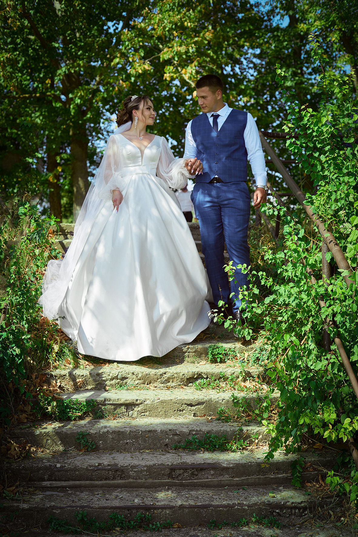 Жених и невеста спускаются вниз по ступенькам среди зеленой растительности. Фотограф. Тимашевск. Кубань. Краснодарский край.