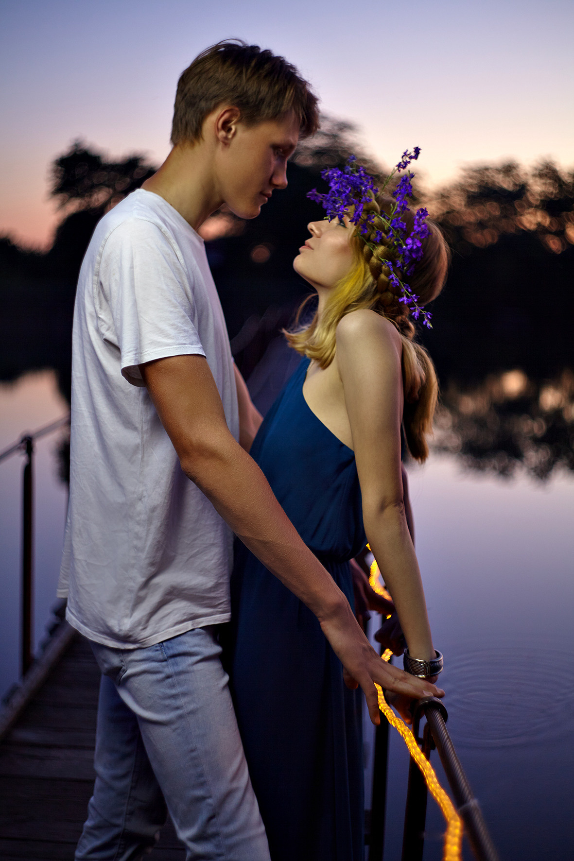 Влюбленная пара на мосту над рекой в часы заката. Парень обнимает девушку с цветочным венком на голове. Фотограф. Тимашевск. Кубань. Краснодарский край.