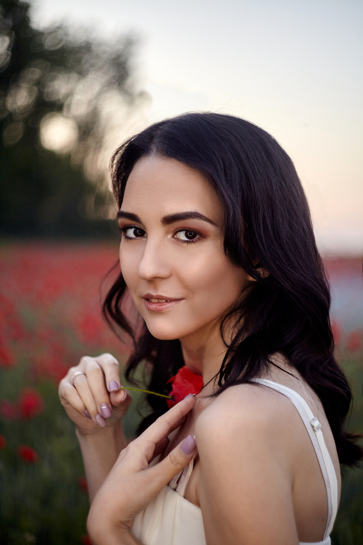 Девушка в белом платье на маковом поле прижимает цветок мака к груди. По маковому полю стелется туман. Фотограф. Тимашевск. Кубань. Краснодарский край.