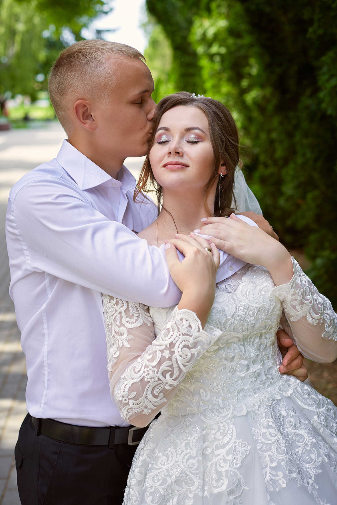 Фотография жениха и невесты в зеленом парке. Жених целует невесту в висок. Фотограф. Тимашевск. Кубань. Краснодарский край.