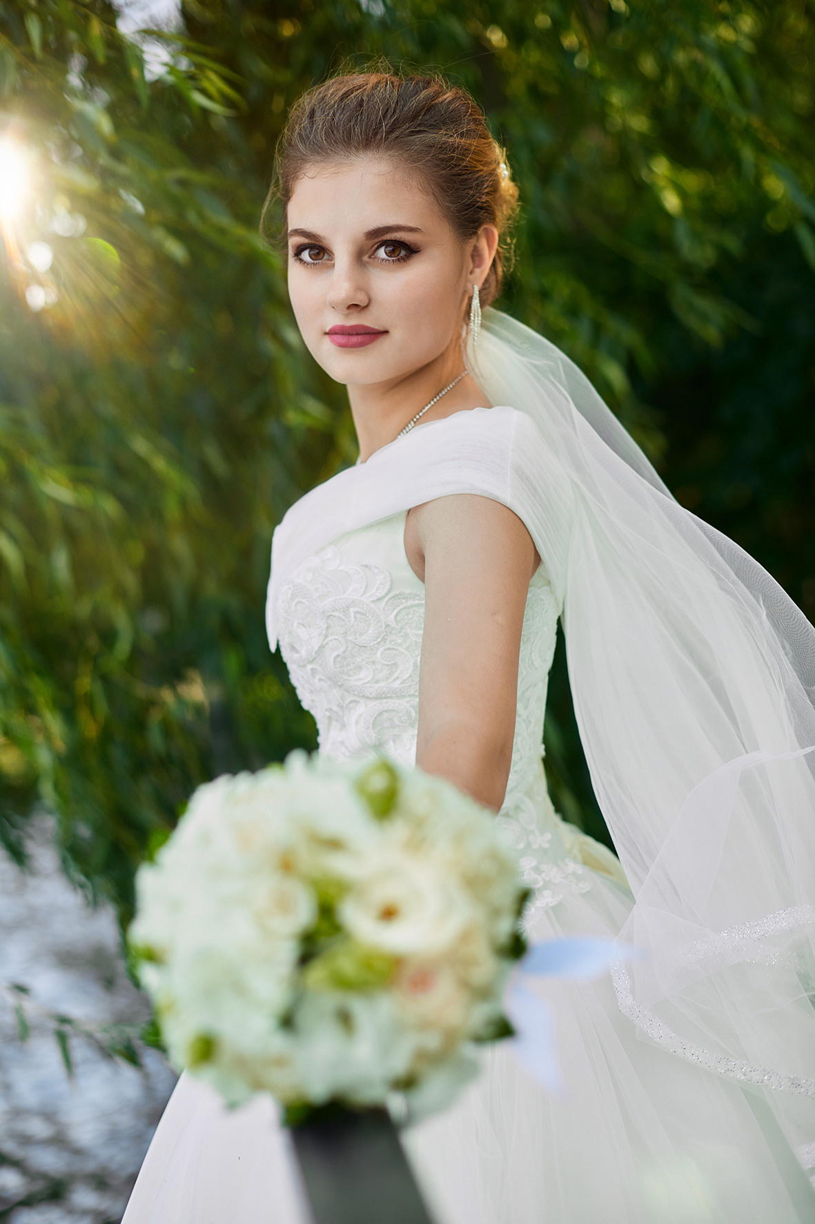 Невеста со свадебным букетом стоит среди зеленой листвы. Фотограф. Кубань. Краснодарский край. Тимашевск.
