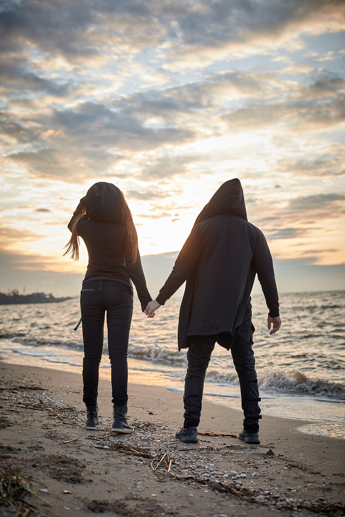 Лавстори на берегу моря во время заката. Море зимой. Песок под ногами. Линия берега и волны. Парень и девушка в черной одежде обнимаются на берегу моря, глядя на закат. Приморско-Ахтарск. Фотограф. Тимашевск. Кубань. Краснодарский край.