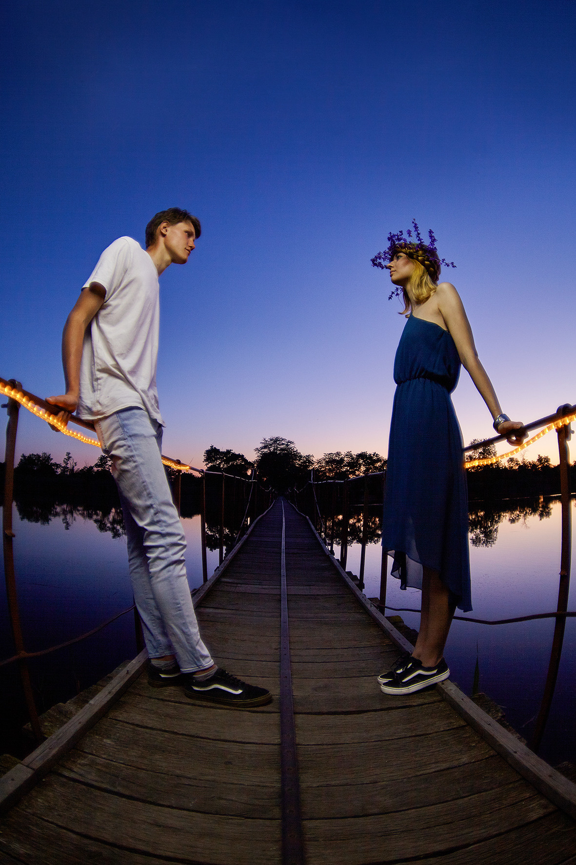 Влюбленная пара на мосту над рекой в часы заката. Парень смотрит на девушку с цветочным венком на голове. Фотограф. Тимашевск. Кубань. Краснодарский край.