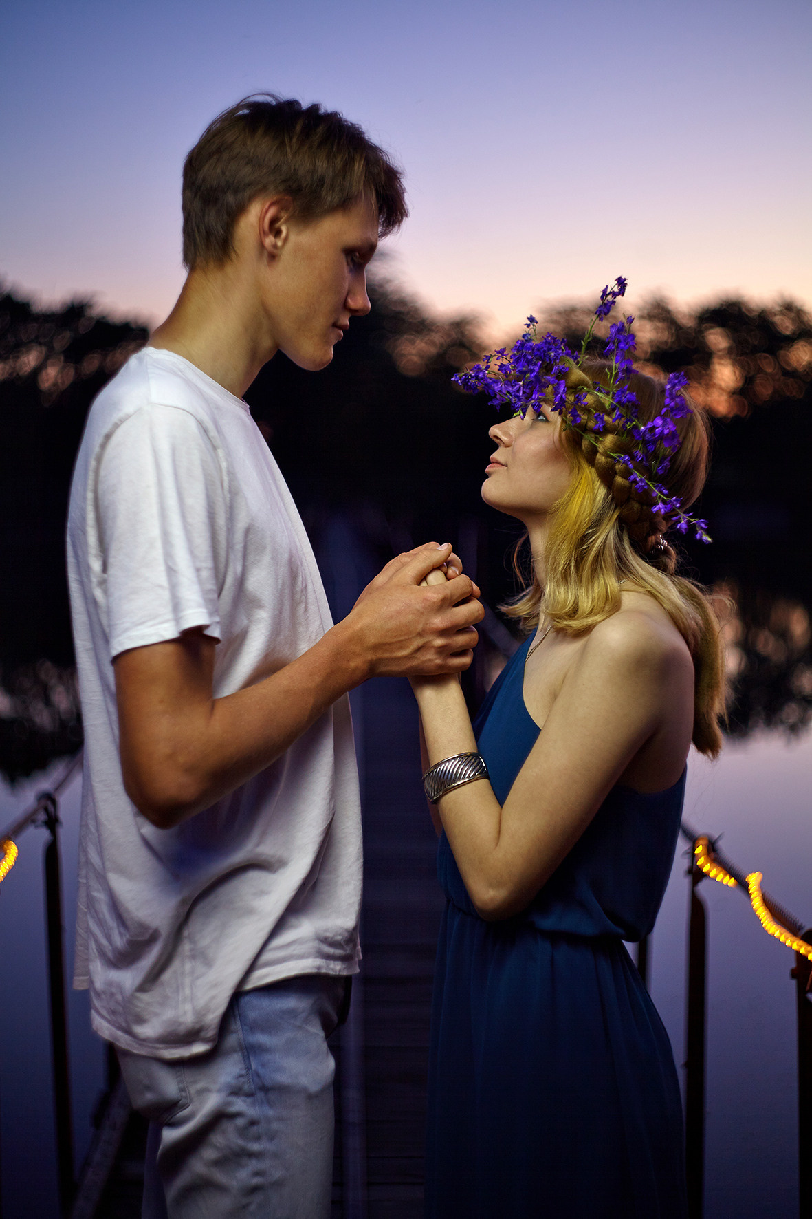 Влюбленная пара на мосту над рекой в часы заката. Парень обнимает девушку с цветочным венком на голове. Фотограф. Тимашевск. Кубань. Краснодарский край.