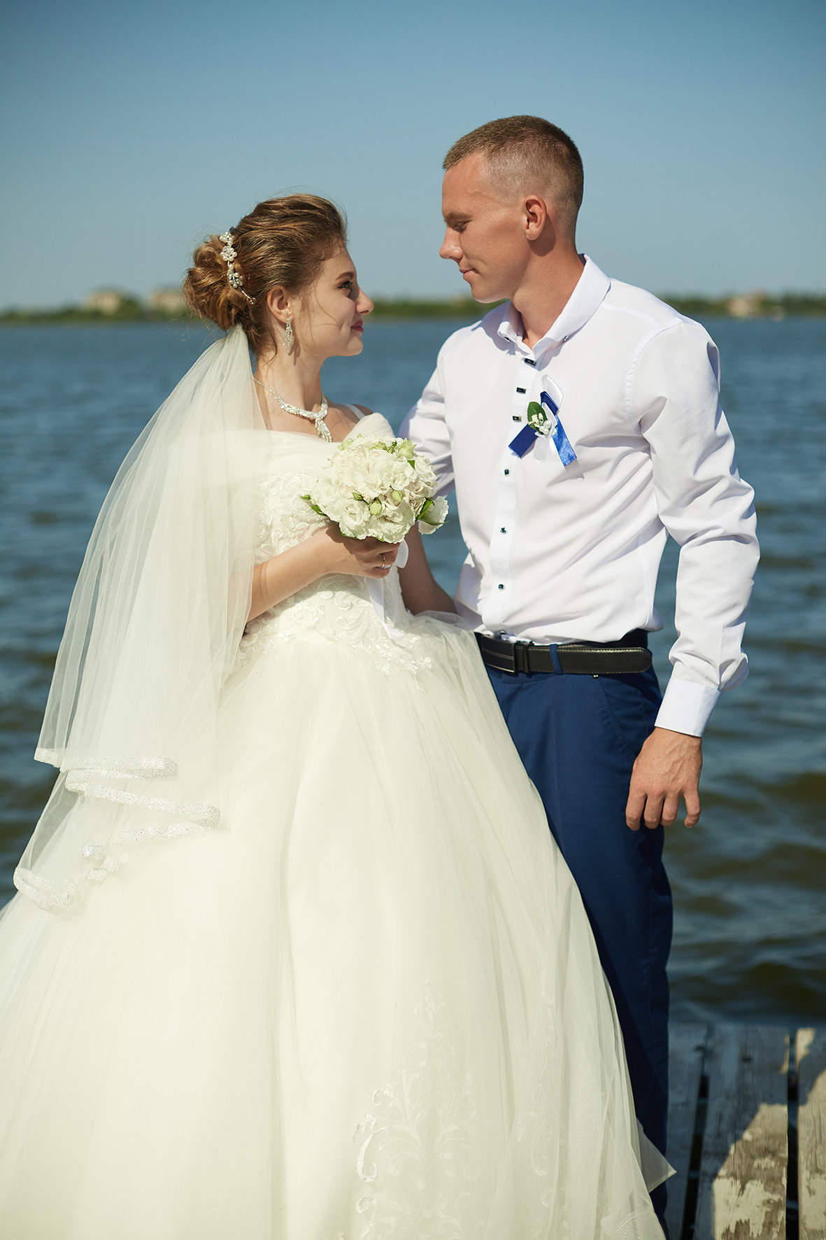 Невеста и жених смотрят друг на друга, стоят на мосту на реке. Фотограф. Кубань. Краснодарский край. Тимашевск.