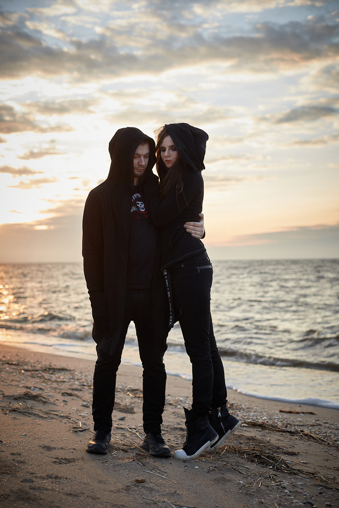 Лавстори на берегу моря во время заката. Море зимой. Песок под ногами. Линия берега и волны. Парень и девушка в черной одежде обнимаются на берегу моря на закате. Приморско-Ахтарск. Фотограф. Тимашевск. Кубань. Краснодарский край.