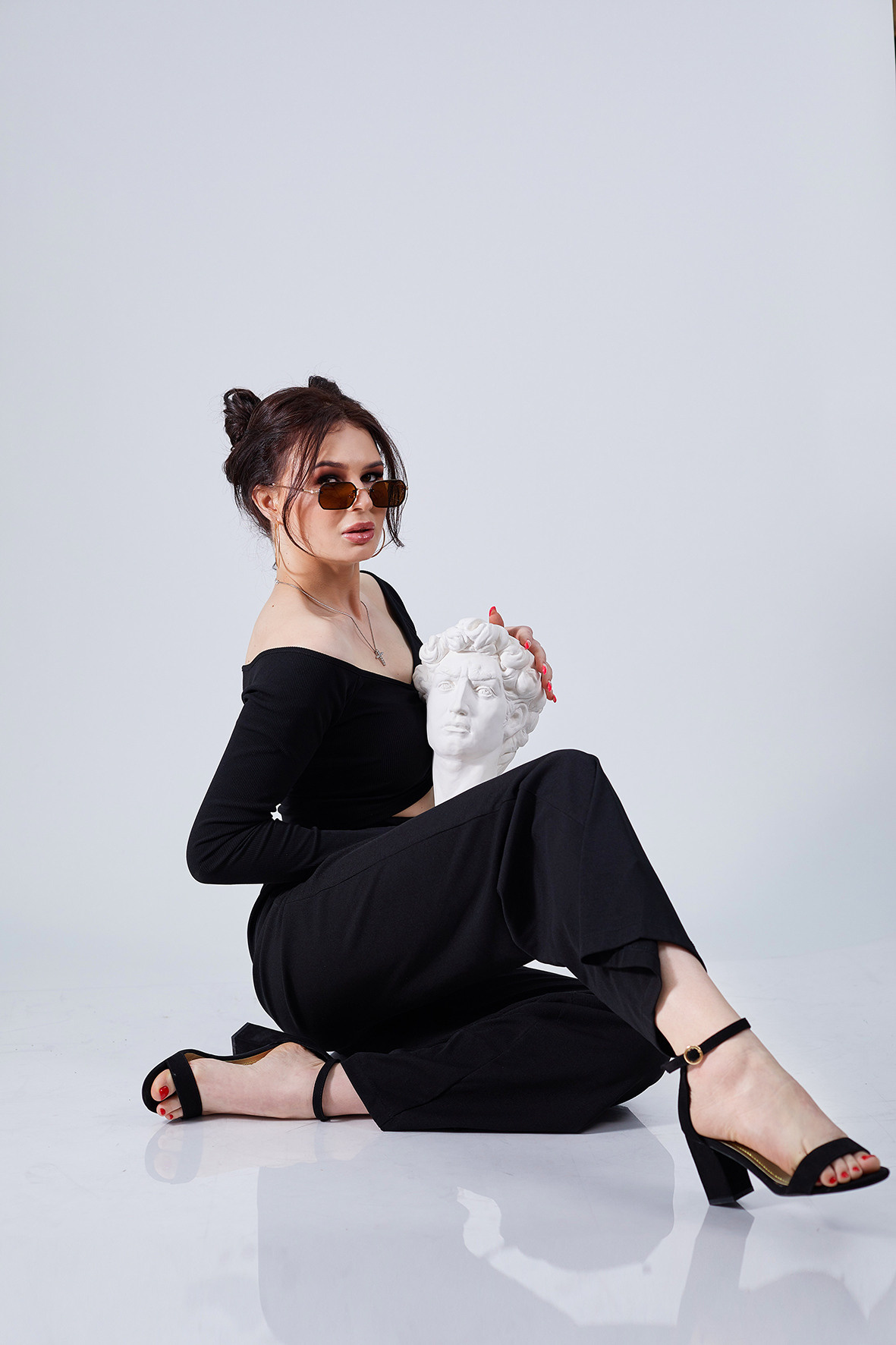 Студийный портрет красивой девушки в черной одежде и солнечных очках. Стильная девушка на белом фоне с гипсовой статуэткой в руках. Фотограф. Тимашевск. Кубань. Краснодарский край.