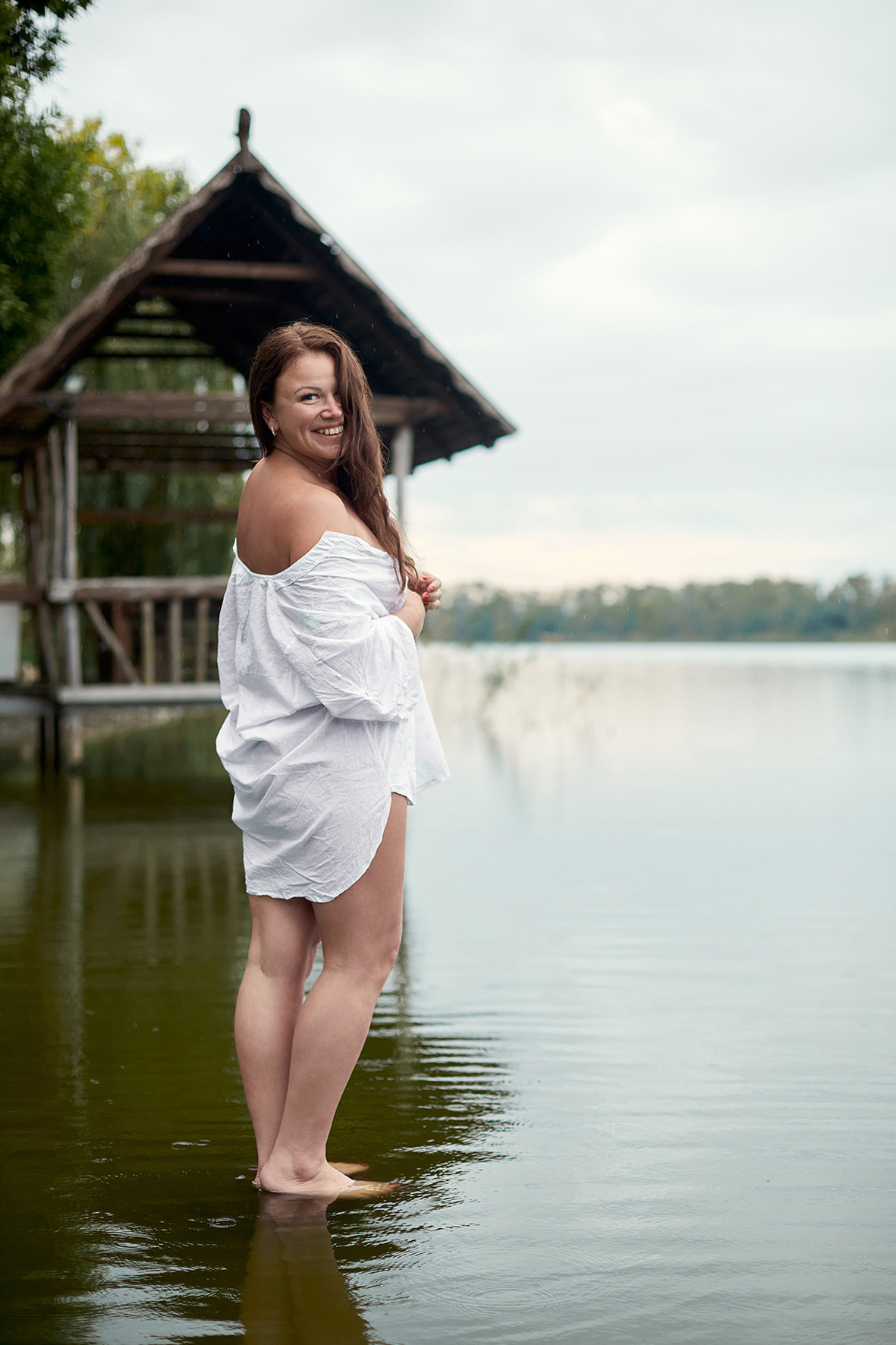 Девушка в белой рубашке стоит на реке на фоне деревянного домика. Фотограф. Тимашевск. Краснодарский край. Кубань.