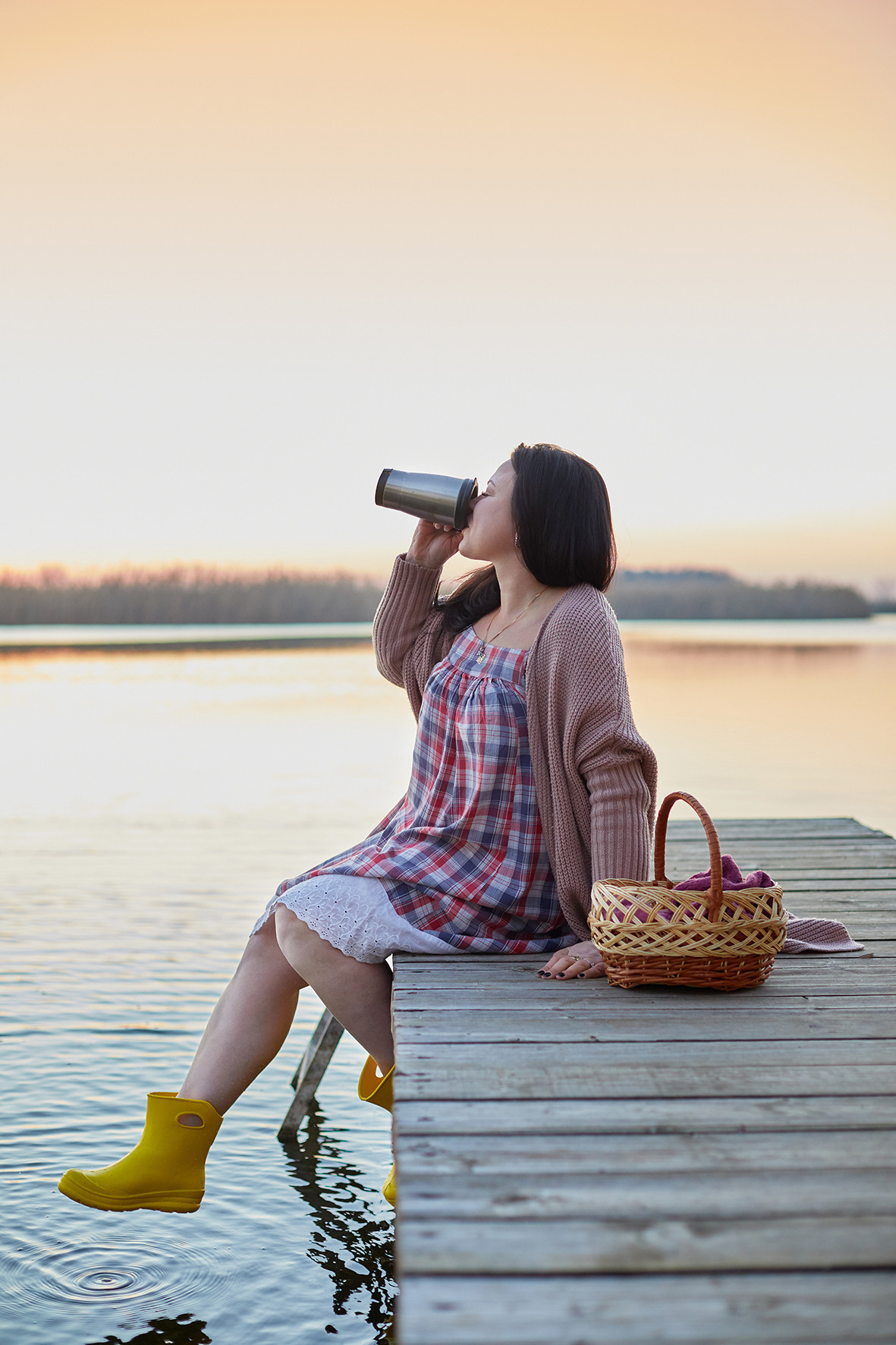 Портрет девушки на реке на закате. Девушка в вязаном кардигане и желтых резиновых сапожках на берегу реки на деревянном пирсе пьет кофе из термоса. Фотограф. Тимашевск. Кубань. Краснодарский край. 