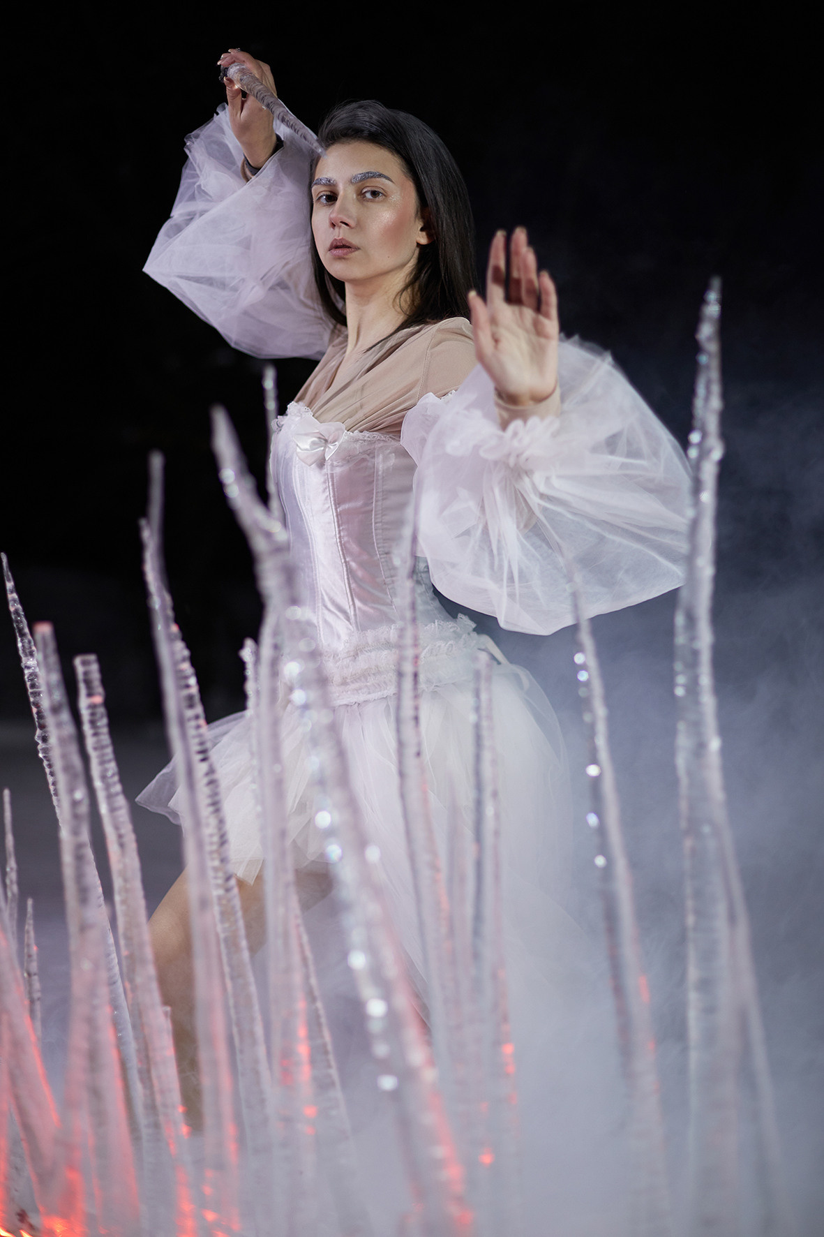 Девушка в белом платье с рукавами-воланами стоит в снегу за изгородью из замерзших сосулек. Сосульки торчат из снега. Снежная королева. Фотограф. Тимашевск. Кубань. Краснодарский край.