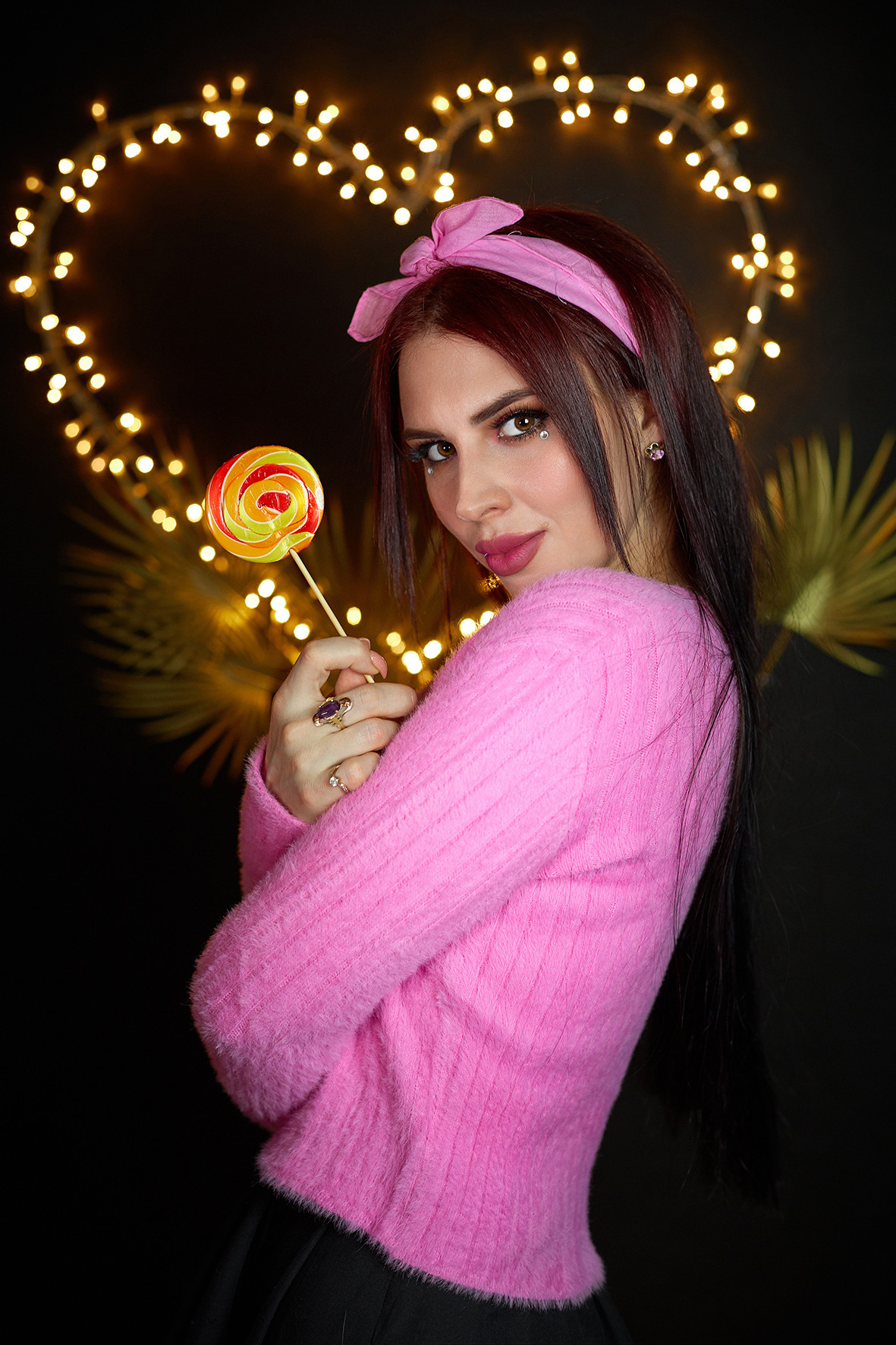 Студийный портрет девушки в розовой кофточке и с розовым платком на голове с карамельным леденцом в руках. Сердце из светодиодов на черном фоне. Фотограф. Тимашевск. Кубань. Краснодарский край.