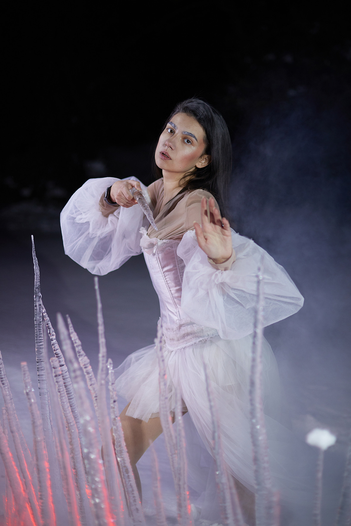 Девушка в белом платье с рукавами-воланами стоит в снегу за изгородью из замерзших сосулек. Сосульки торчат из снега. Снежная королева. Фотограф. Тимашевск. Кубань. Краснодарский край.