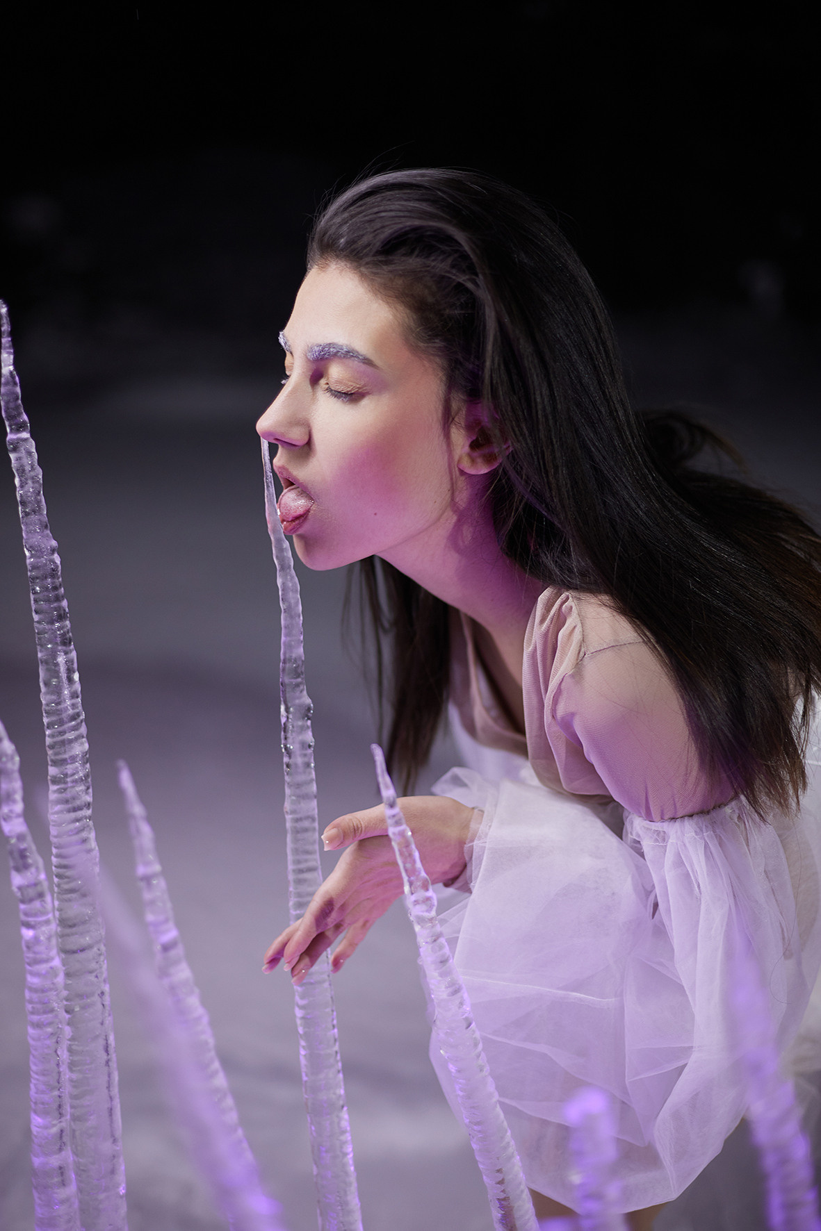 Девушка в белом платье с рукавами-воланами стоит в снегу за изгородью из замерзших сосулек. Сосульки торчат из снега. Девушка облизывает большую сосульку. Снежная королева. Фотограф. Тимашевск. Кубань. Краснодарский край.