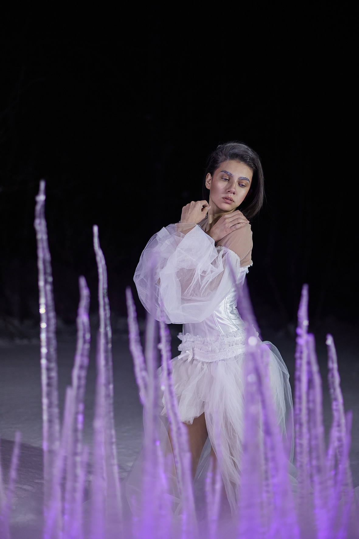 Девушка в белом платье с рукавами-воланами стоит в снегу за изгородью из замерзших сосулек. Сосульки торчат из снега. Снежная королева. Фотограф. Тимашевск. Кубань. Краснодарский край.