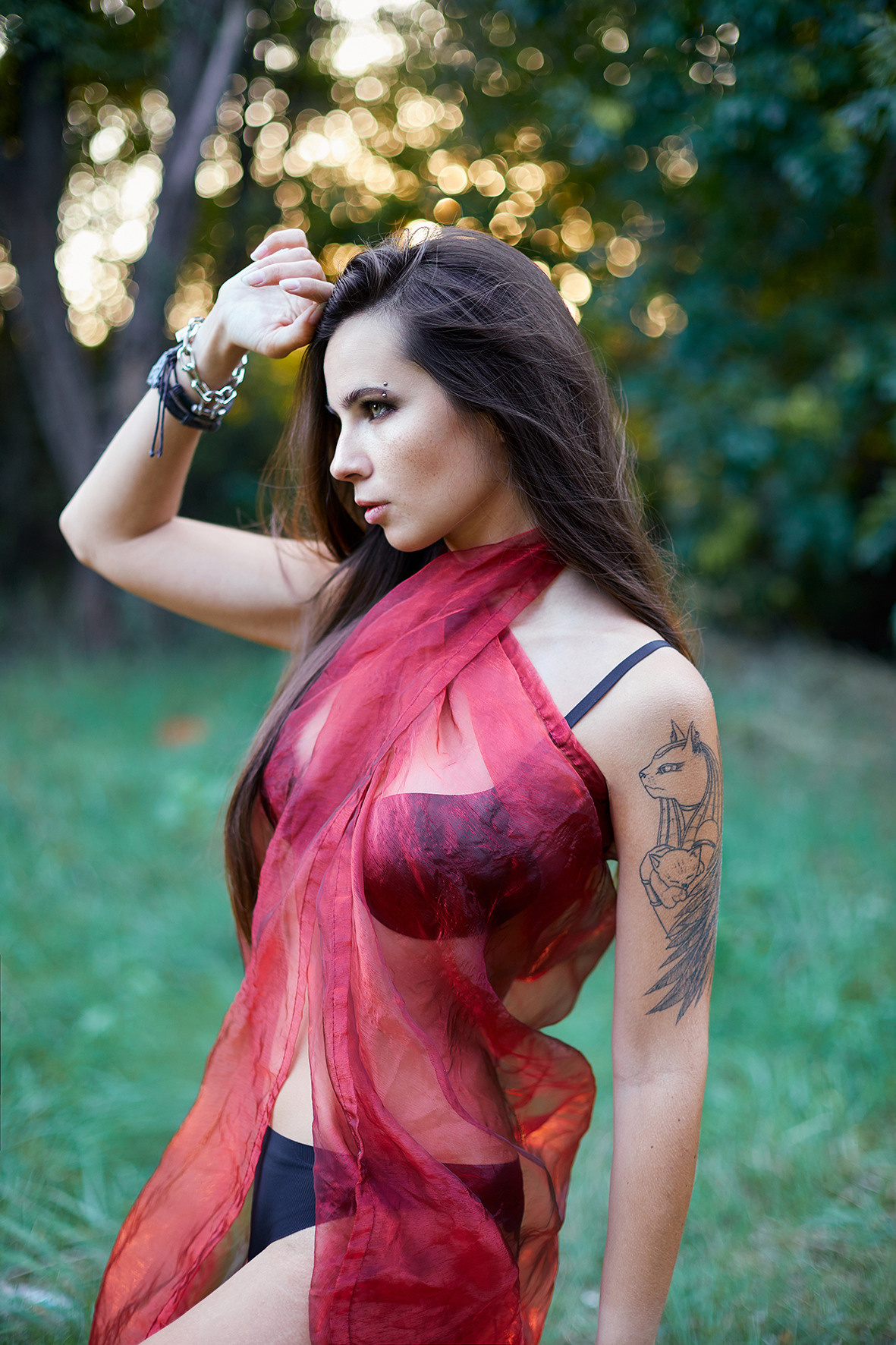 Девушка с татуировками в черном белье и красном платке на тело стоит на лесной поляне в час заката. Фотограф. Тимашевск. Кубань. Краснодарский край.