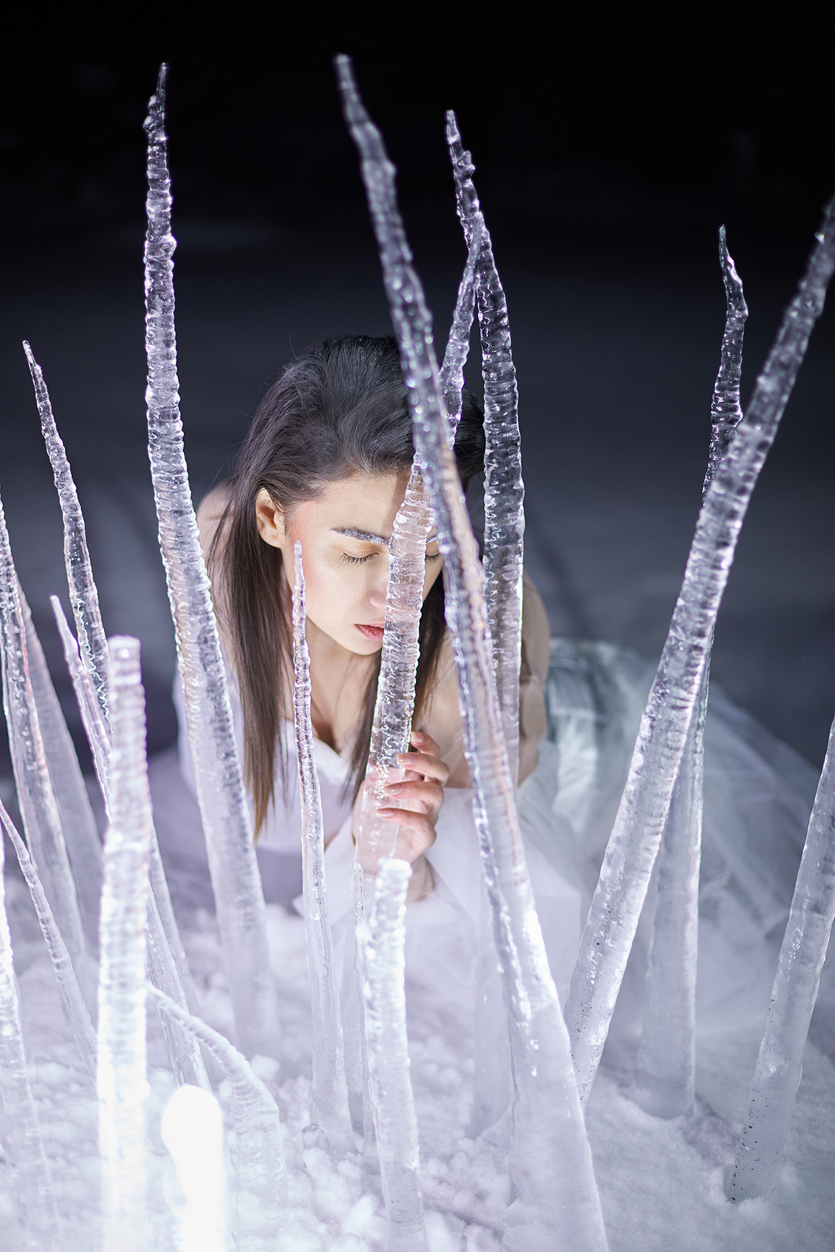 Девушка в белом платье с рукавами-воланами стоит в снегу за изгородью из замерзших сосулек. Сосульки торчат из снега. Снежная королева. Фотограф. Тимашевск. Кубань. Краснодарский край.