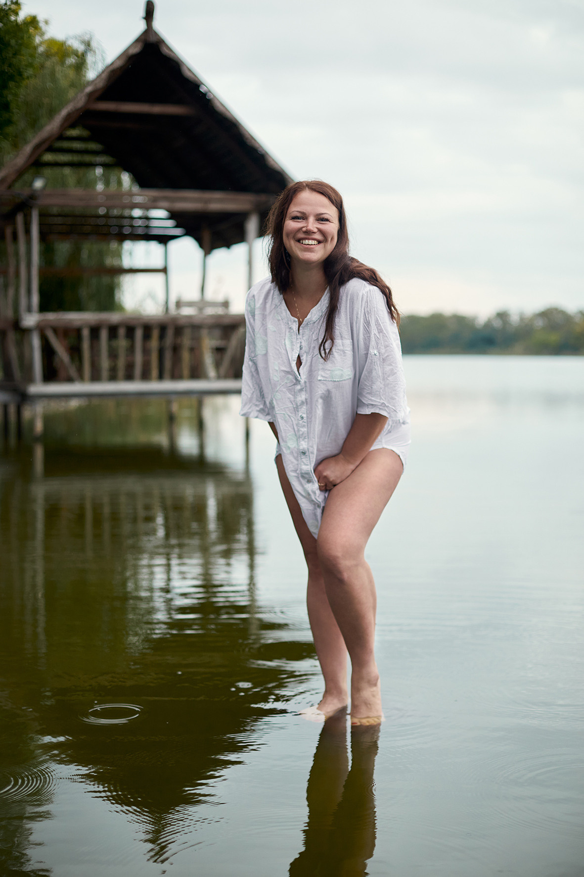 Девушка в белой рубашке стоит на реке на фоне деревянного домика. Фотограф. Тимашевск. Краснодарский край. Кубань.