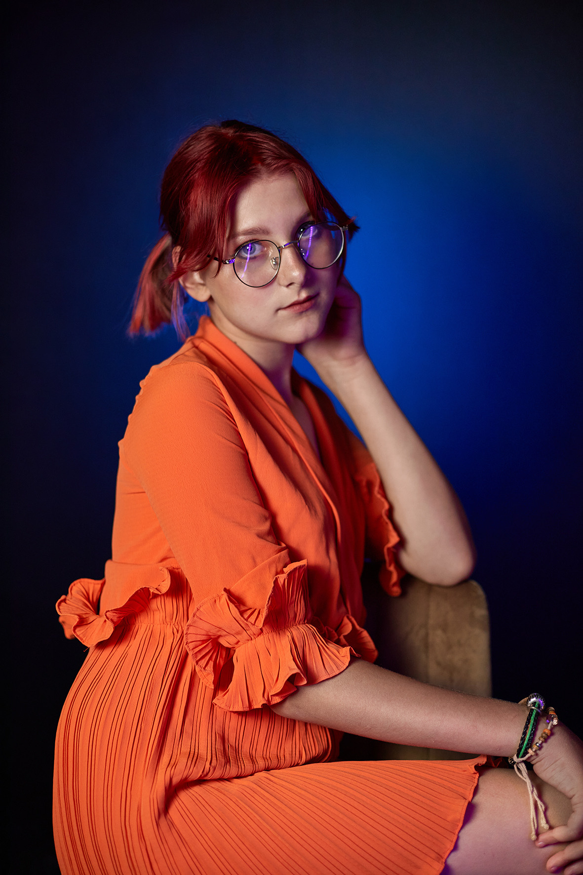 Студийный портрет девочки в очках с красными волосами в оранжевом платье на синем фоне. Фотограф. Тимашевск. Кубань. Краснодарский край.