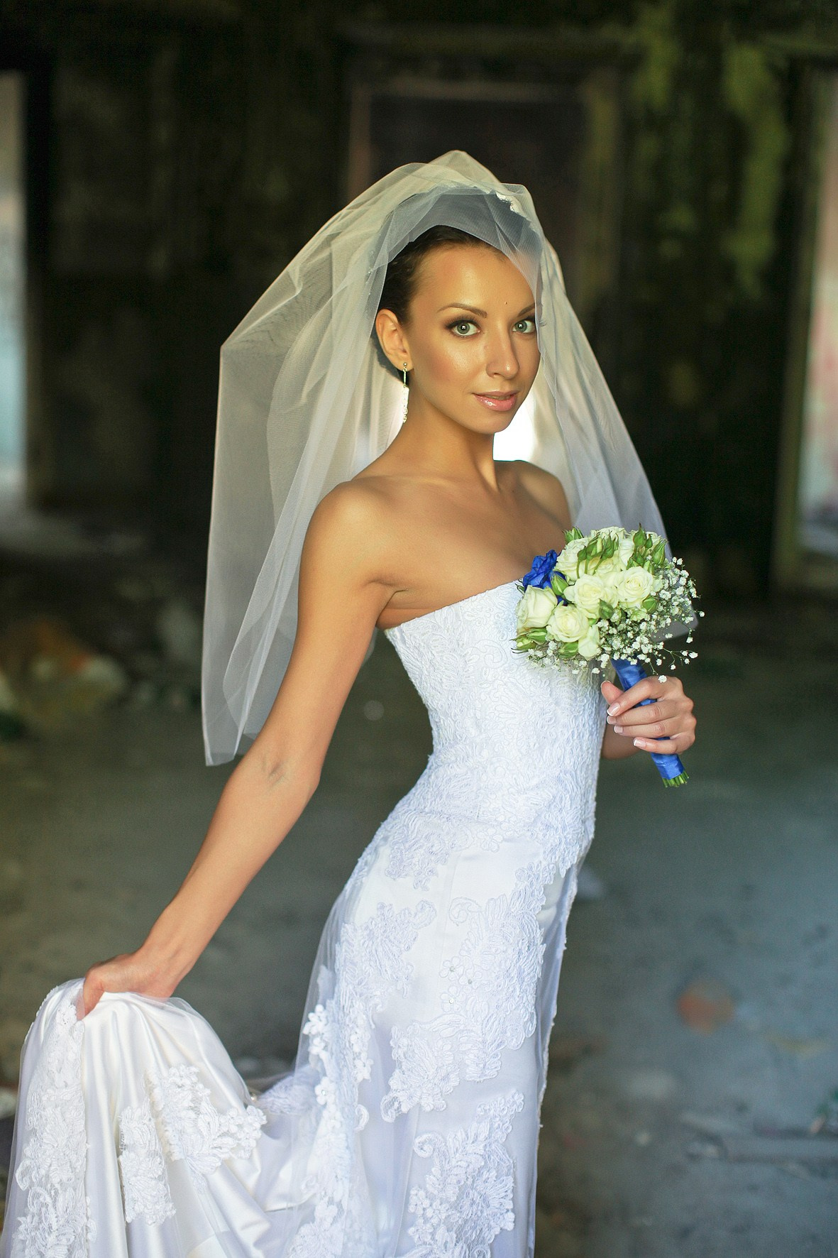 невеста в американской фате с синим букетом держит рукой подол платья 