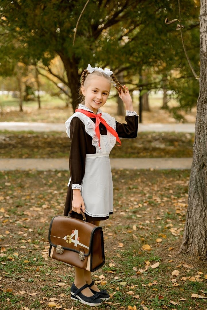 Юная школьница позирует с портфелем на камеру фотографу в осеннем лесу.