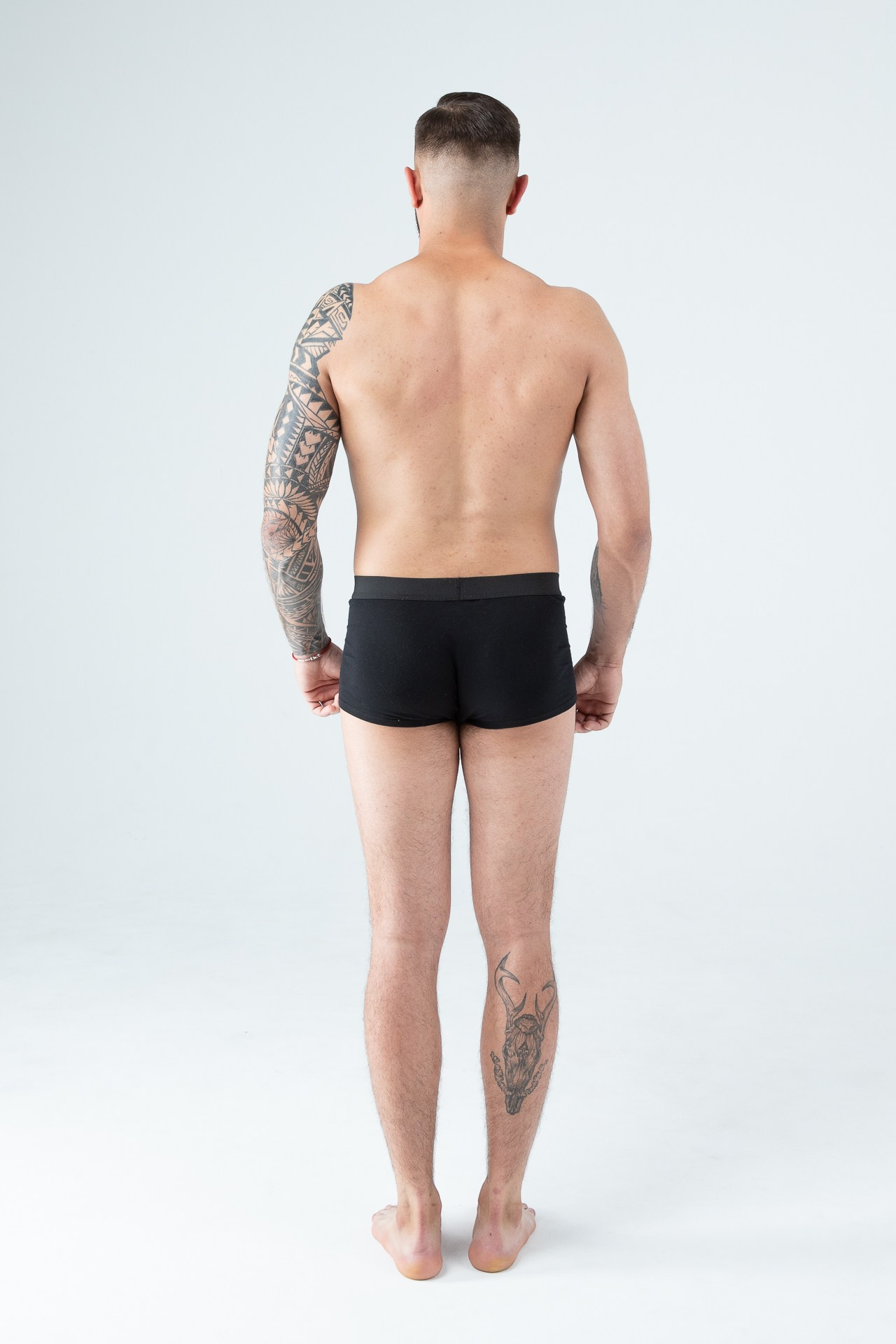Мужчина модель с бородой с татуировками в черных трусах