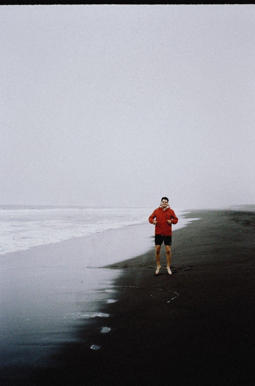 Мужчина радостно прыгает на черном песке Халактырского пляжа Камчатки