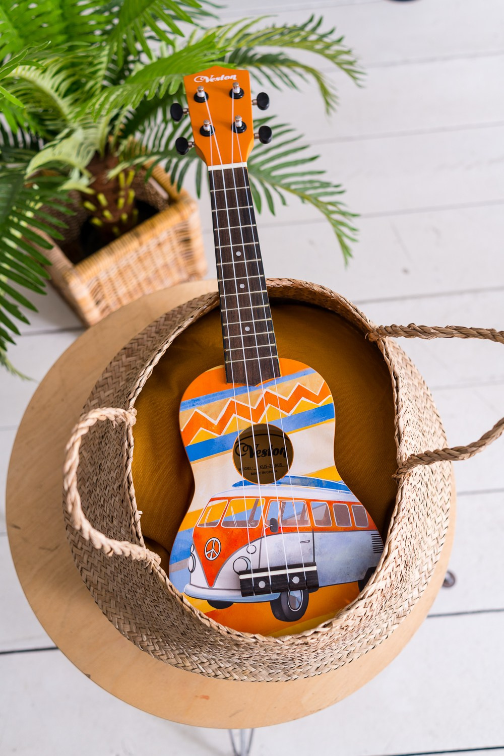 Разноцветная укулеле лежит в соломенной корзине на столе
