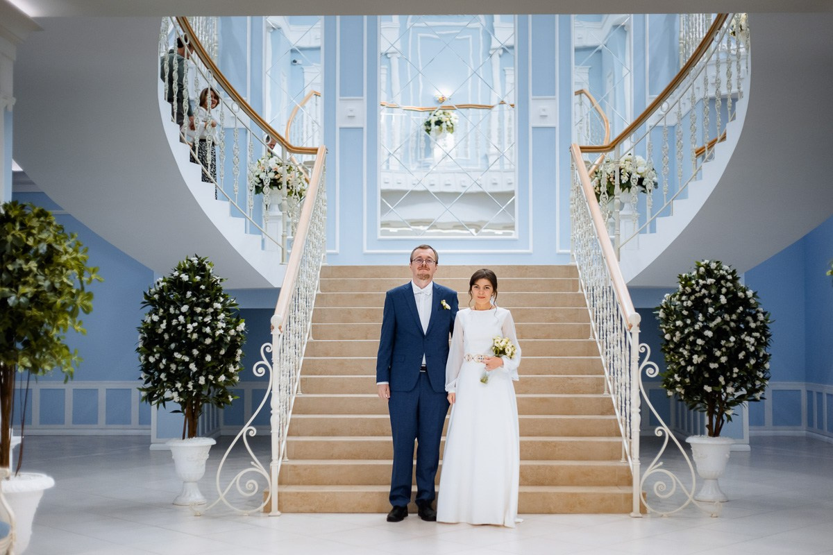 Жених и невеста стоят перед лестницей в холе ЗАГСа Красносельского района Санкт-Петербурга. Общий план.